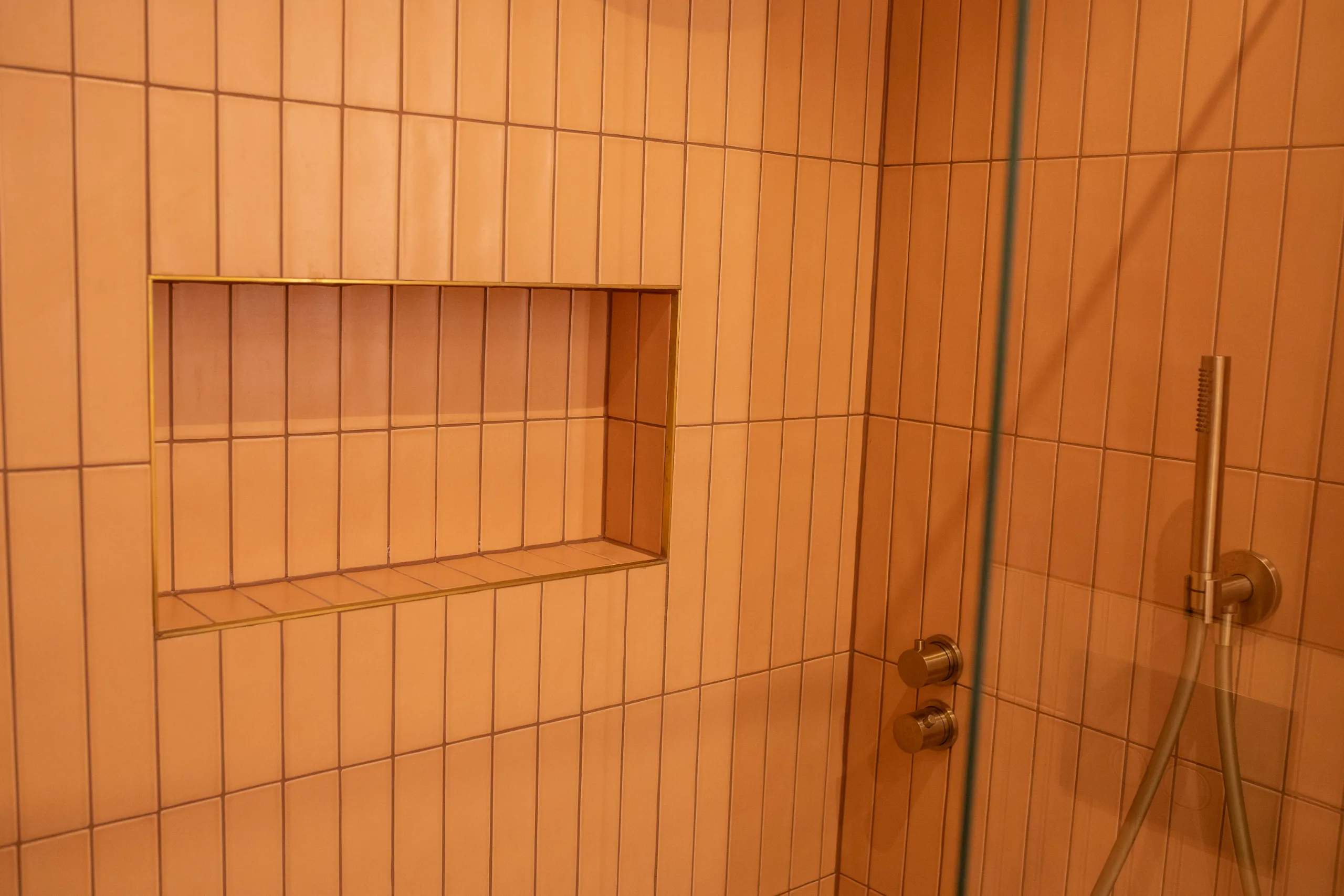 Moderni kylpyhuone, jossa pitkät roosan väriset laatat ja shampanjansävyiset suihkukalusteet